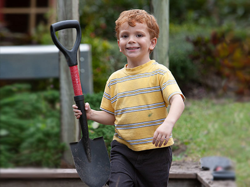 boy holding a shovel outdoors at Bridges Montessori school